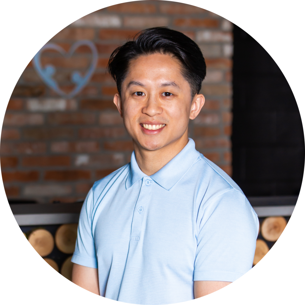 A man in a blue shirt smiling in front of a brick wall.